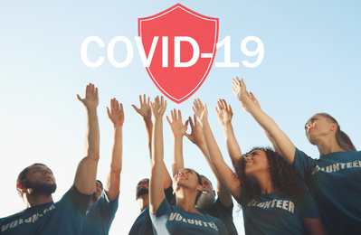 Image of Volunteers uniting to help during COVID-19 outbreak. Group of people raising hands outdoors, shield illustration 