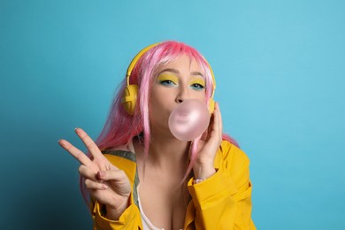 Photo of Fashionable young woman in pink wig with headphones blowing bubblegum on yellow background