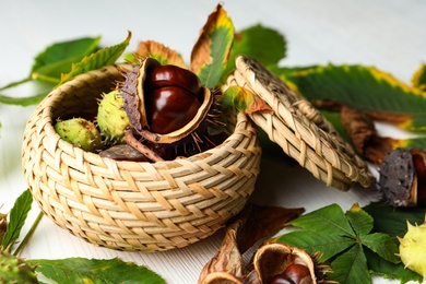 Photo of Horse chestnuts in wicker basket on white wooden table, closeup