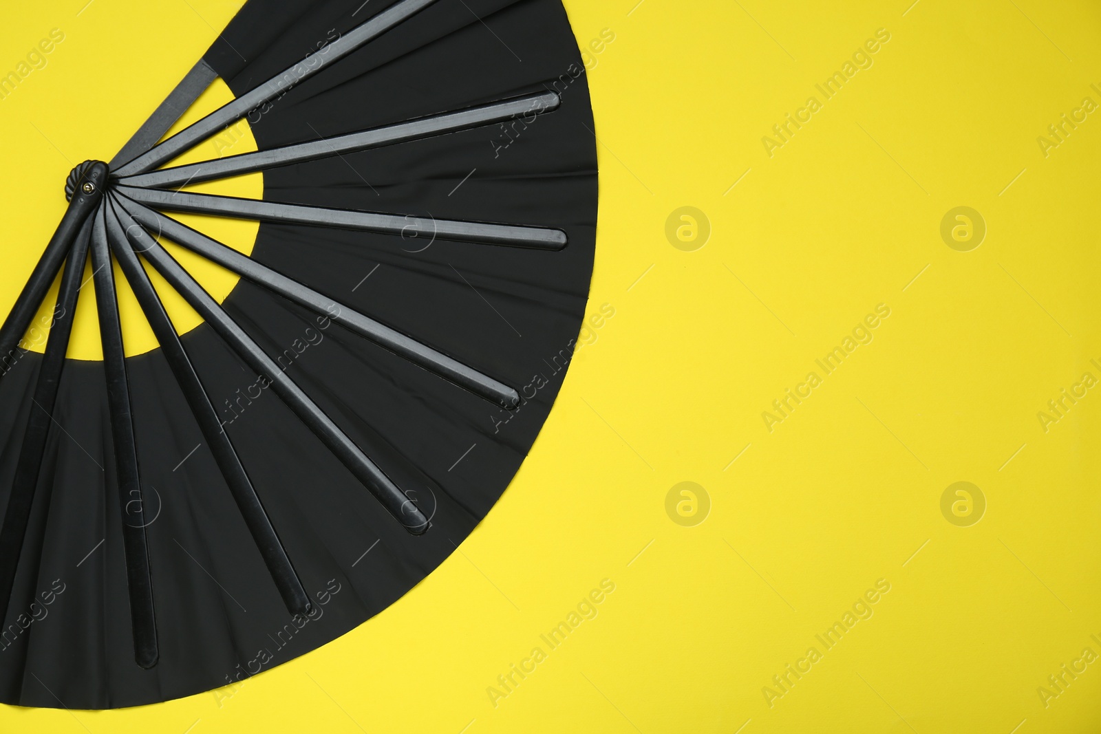 Photo of Stylish black hand fan on yellow background, top view. Space for text