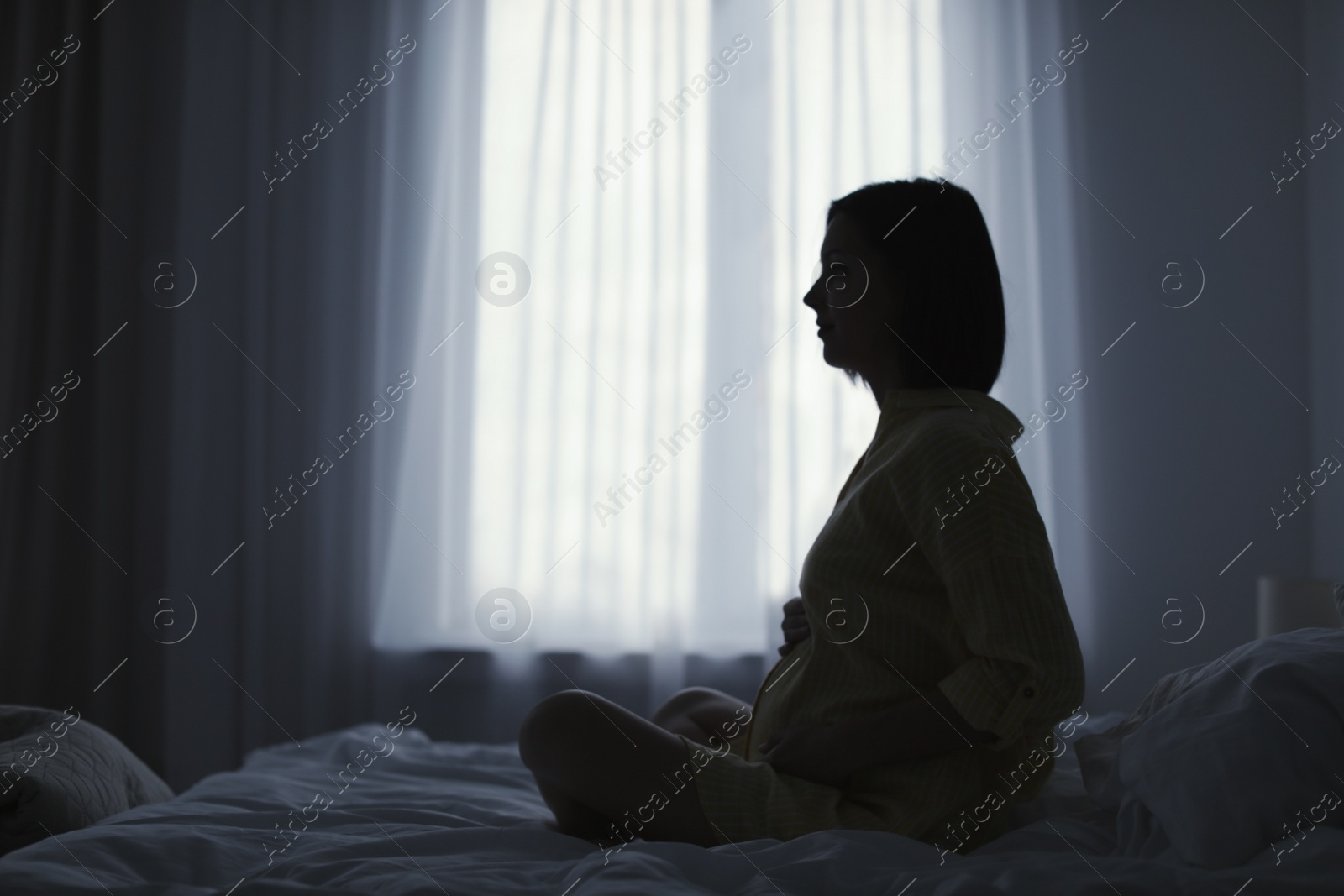 Photo of Beautiful pregnant woman sitting on bed at home