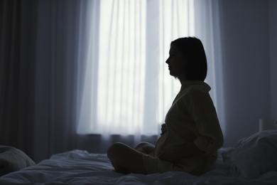 Beautiful pregnant woman sitting on bed at home