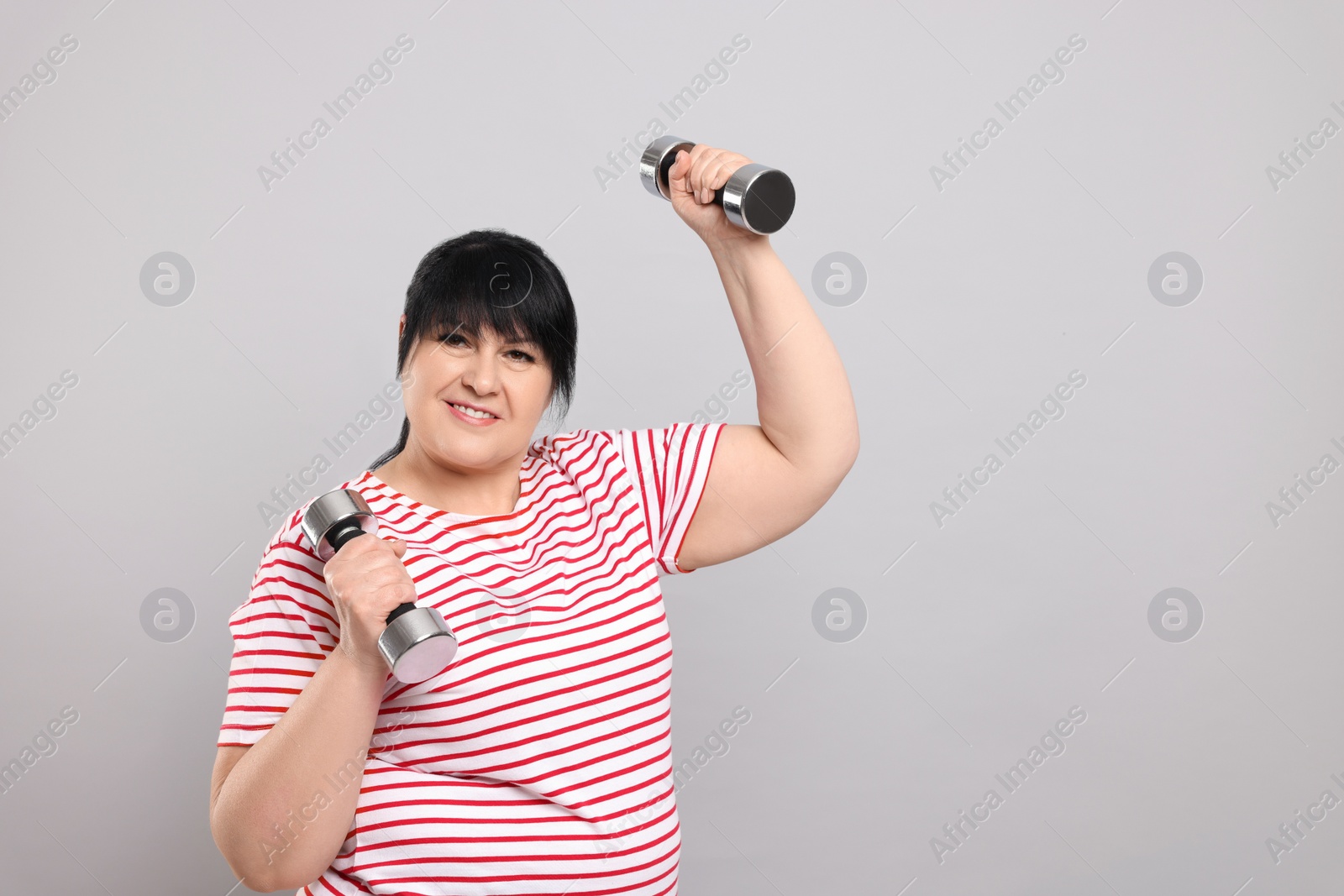 Photo of Happy overweight mature woman doing exercise with dumbbells on grey background. Space for text