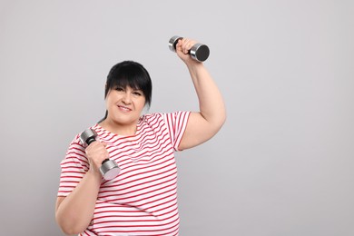 Photo of Happy overweight mature woman doing exercise with dumbbells on grey background. Space for text