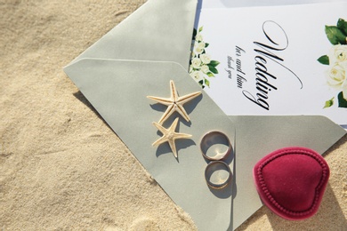 Photo of Flat lay composition with wedding invitation and gold rings on sandy beach