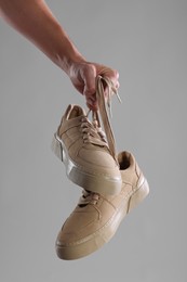 Man holding stylish sneakers on light grey background, closeup