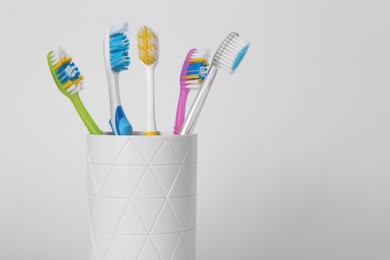 Photo of Different toothbrushes in holder on light grey background, closeup. Space for text