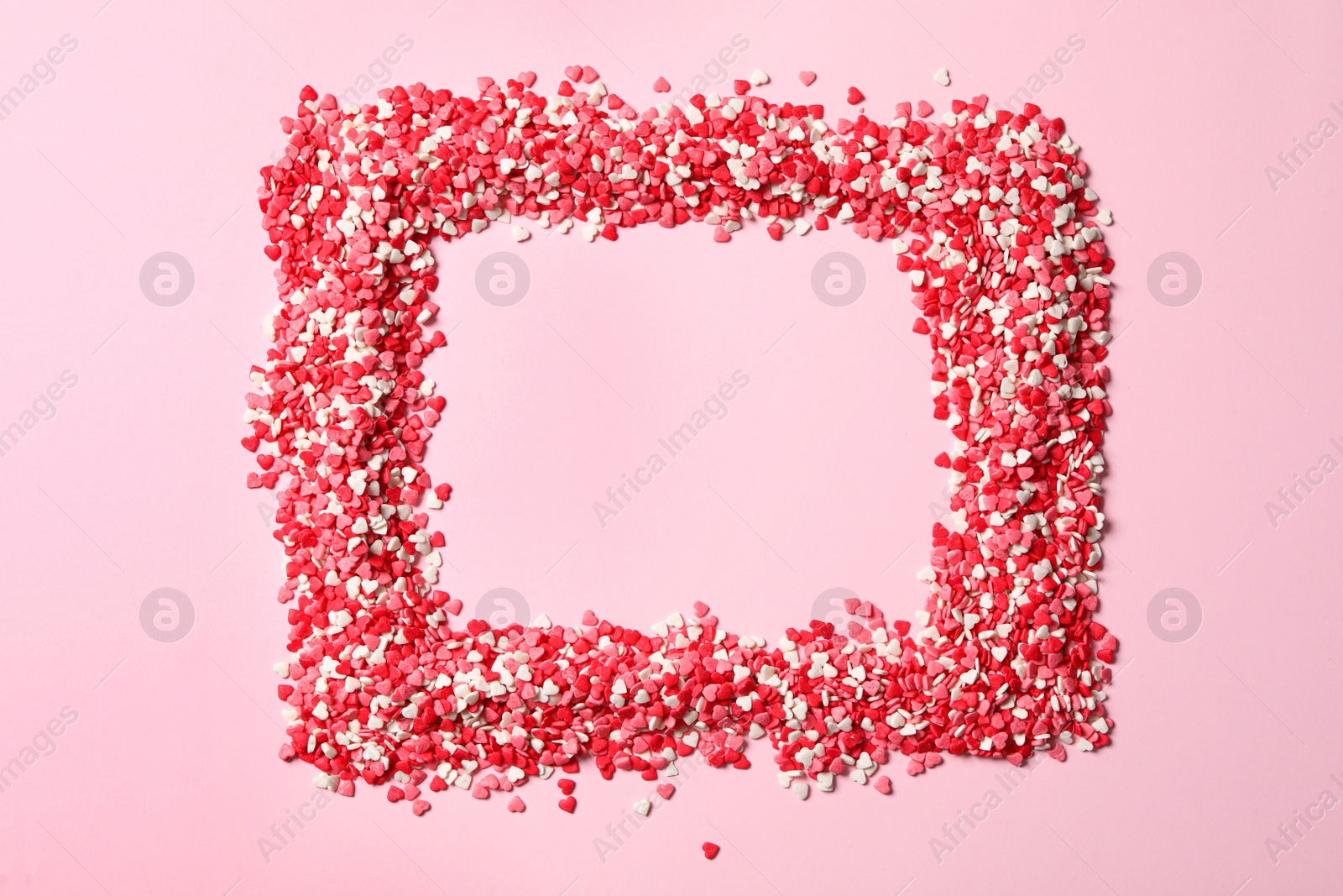 Photo of Frame made of heart shaped sprinkles on pink background, top view. Space for text