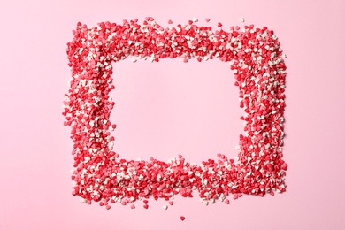 Frame made of heart shaped sprinkles on pink background, top view. Space for text