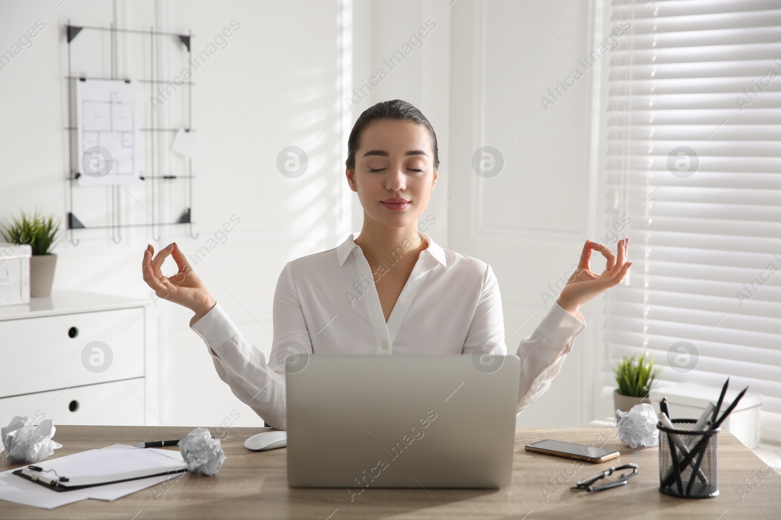 Photo of Young businesswoman meditating at workplace. Stress relief exercise