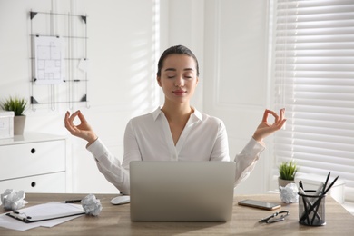 Photo of Young businesswoman meditating at workplace. Stress relief exercise