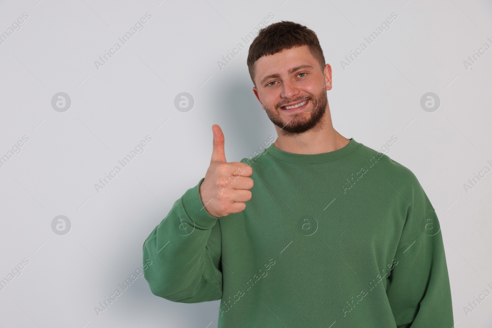 Photo of Young man showing thumb up on white background, space for text