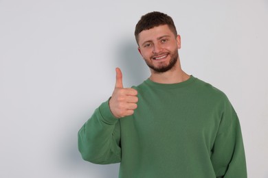 Young man showing thumb up on white background, space for text