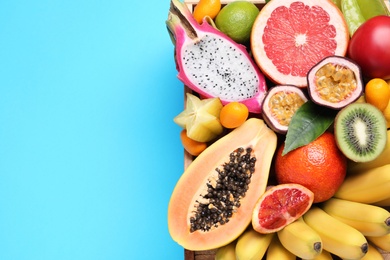 Crate with different exotic fruits on light blue background, top view. Space for text