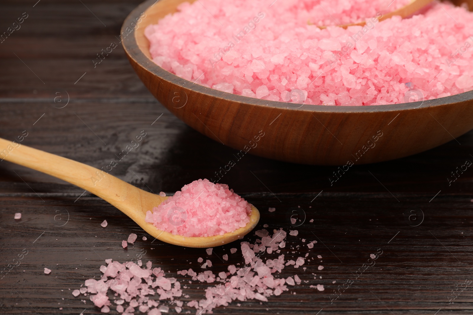 Photo of Bowl and spoon with pink sea salt on wooden table, closeup