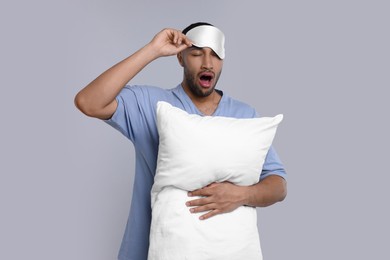 Photo of Man with pillow and sleep mask yawning on light grey background. Insomnia problem