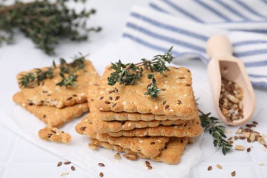 Cereal crackers with flax, sesame seeds and thyme on white tiled table, closeup