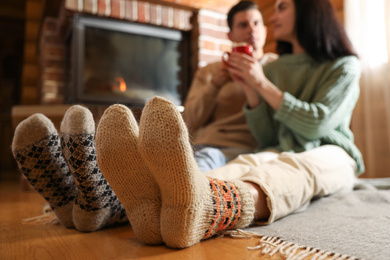 Photo of Lovely couple with delicious cocoa near fireplace at home, focus on feet. Winter vacation