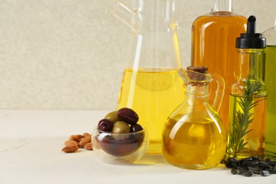 Vegetable fats. Different cooking oils in glass bottles and ingredients on white table, space for text