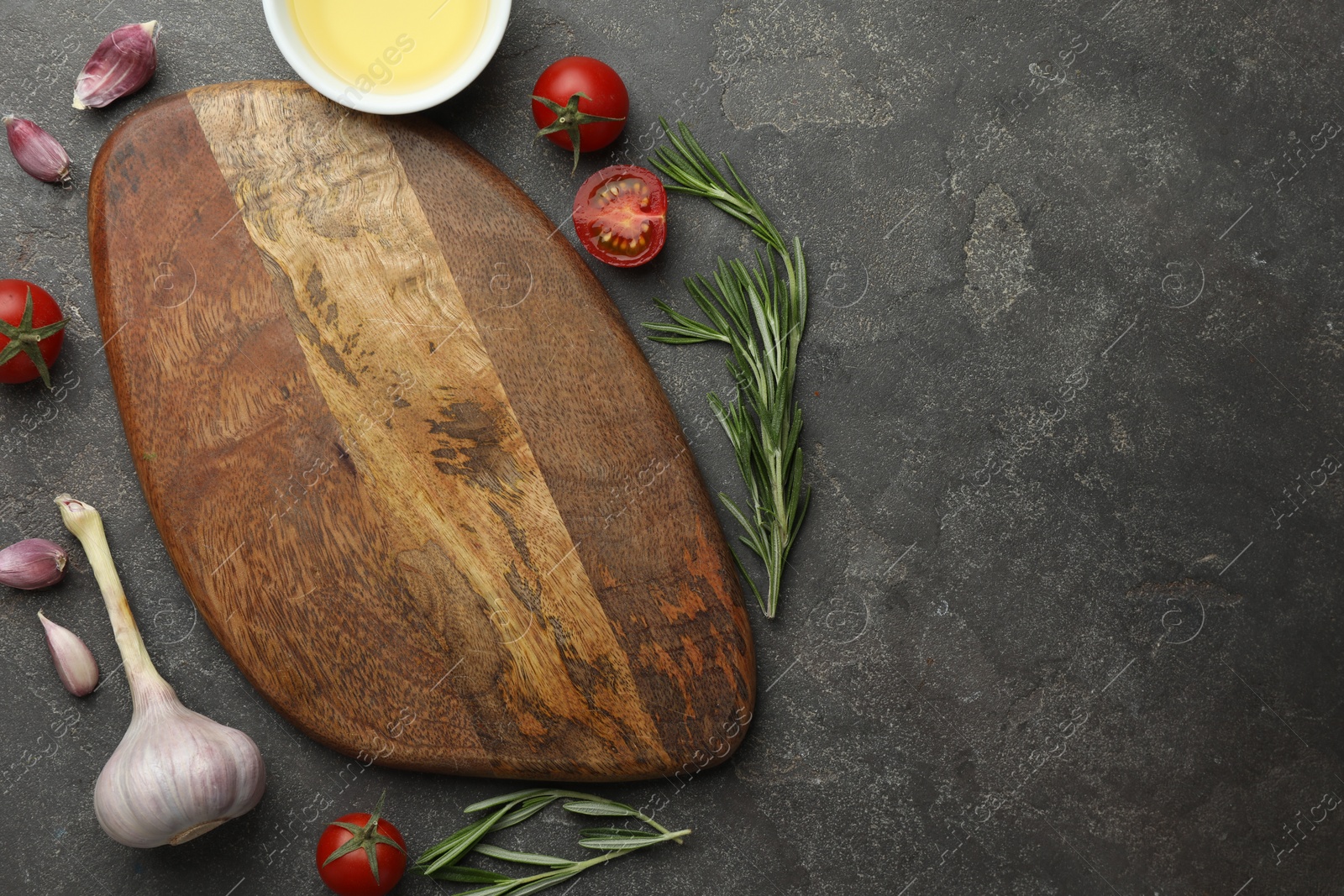 Photo of Cutting board, rosemary, garlic, oil and tomatoes on black table, flat lay. Space for text