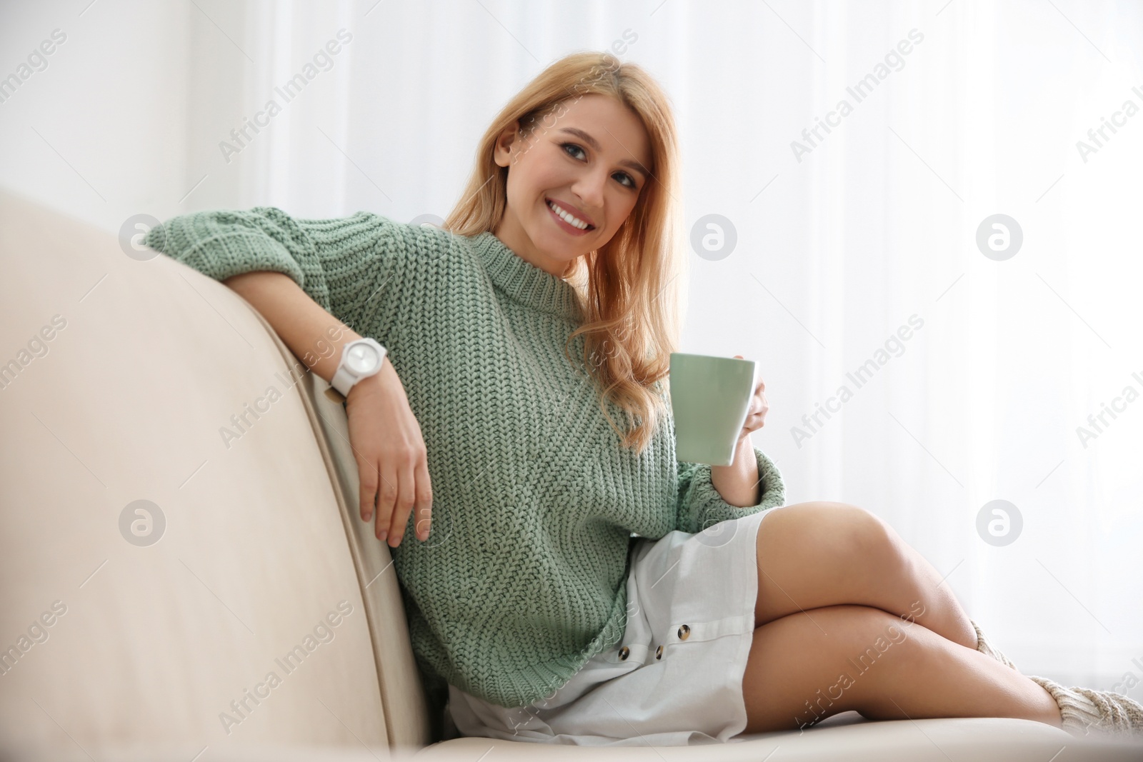 Photo of Young woman with cup of drink relaxing on couch near window at home