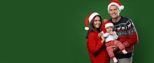 Happy couple with cute baby in Christmas outfits and Santa hats on green background