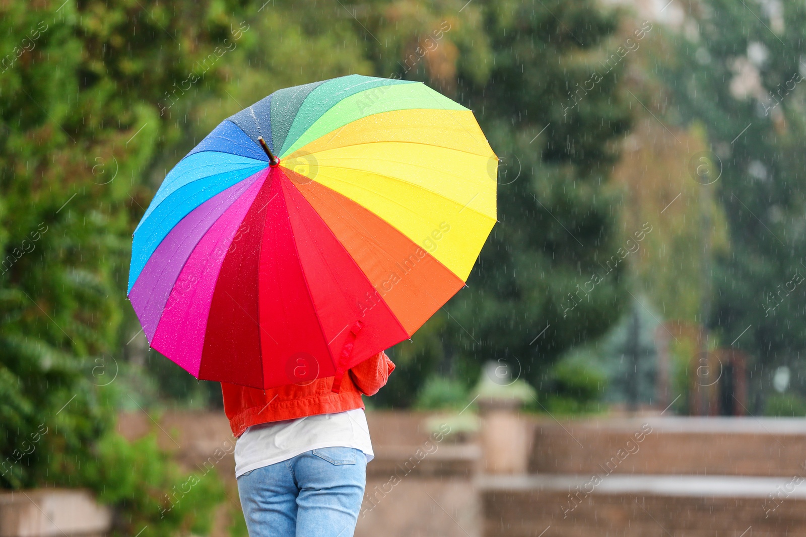 Photo of Young woman with bright umbrella under rain outdoors