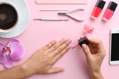 Woman applying nail polish on color background, above view