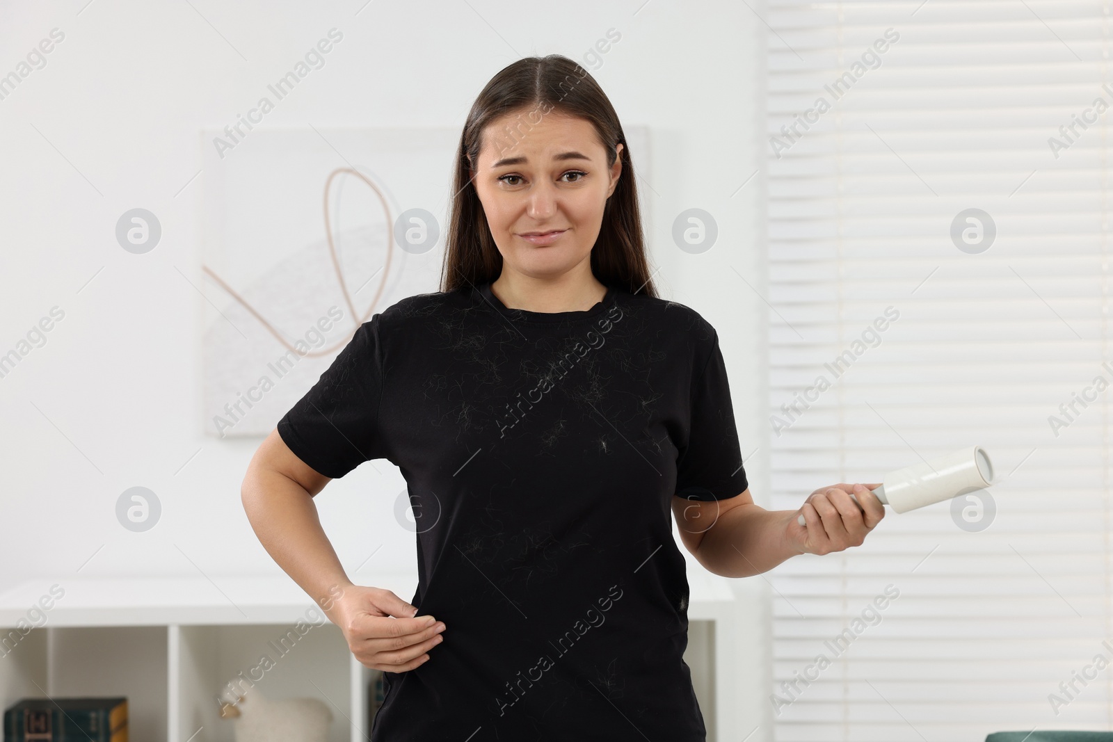 Photo of Emotional woman with lint roller and pet hair on her black clothers at home