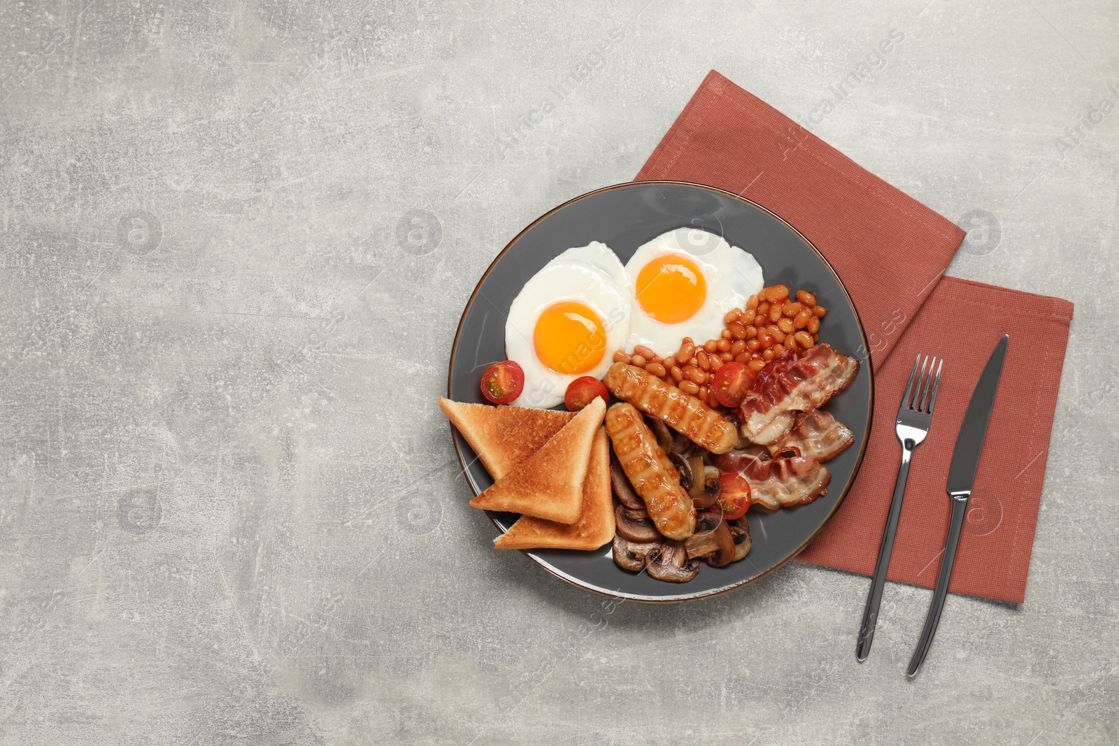 Photo of Plate of fried eggs, sausages, mushrooms, beans, bacon and toasted bread on grey table, flat lay with space for text. Traditional English breakfast
