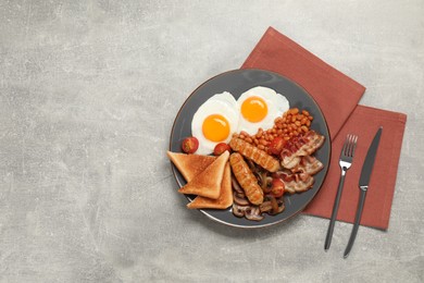 Plate of fried eggs, sausages, mushrooms, beans, bacon and toasted bread on grey table, flat lay with space for text. Traditional English breakfast