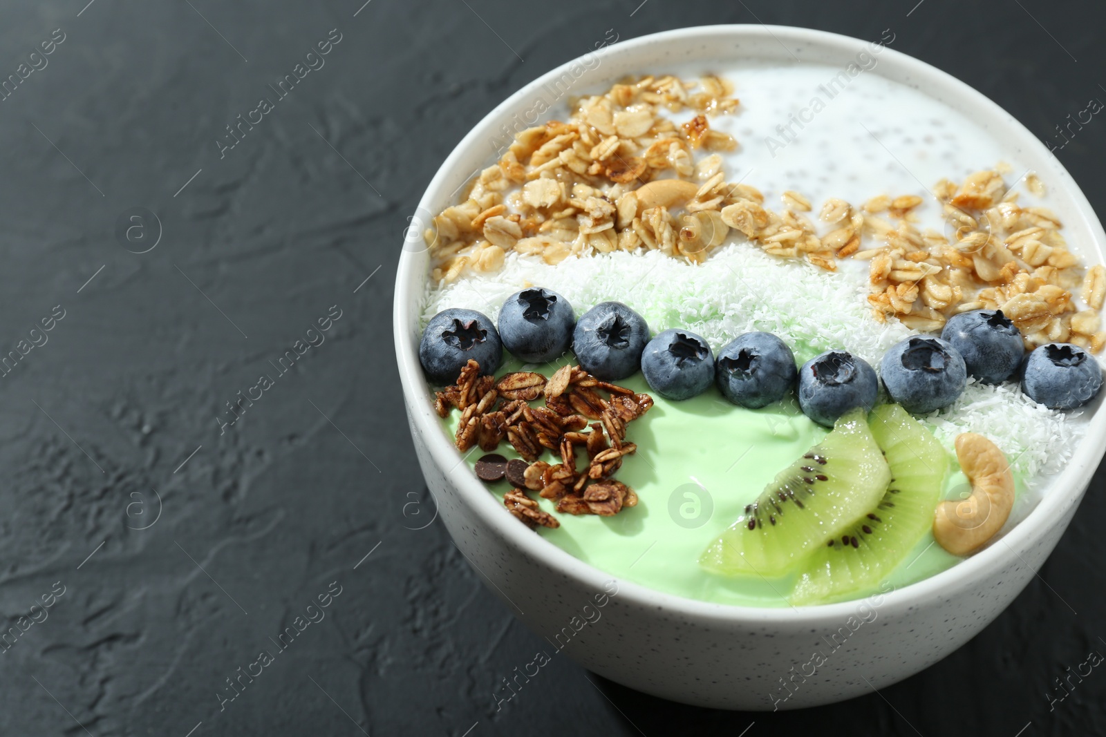 Photo of Tasty smoothie bowl with fresh kiwi fruit, blueberries and oatmeal on black table, closeup. Space for text