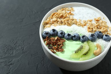 Tasty smoothie bowl with fresh kiwi fruit, blueberries and oatmeal on black table, closeup. Space for text