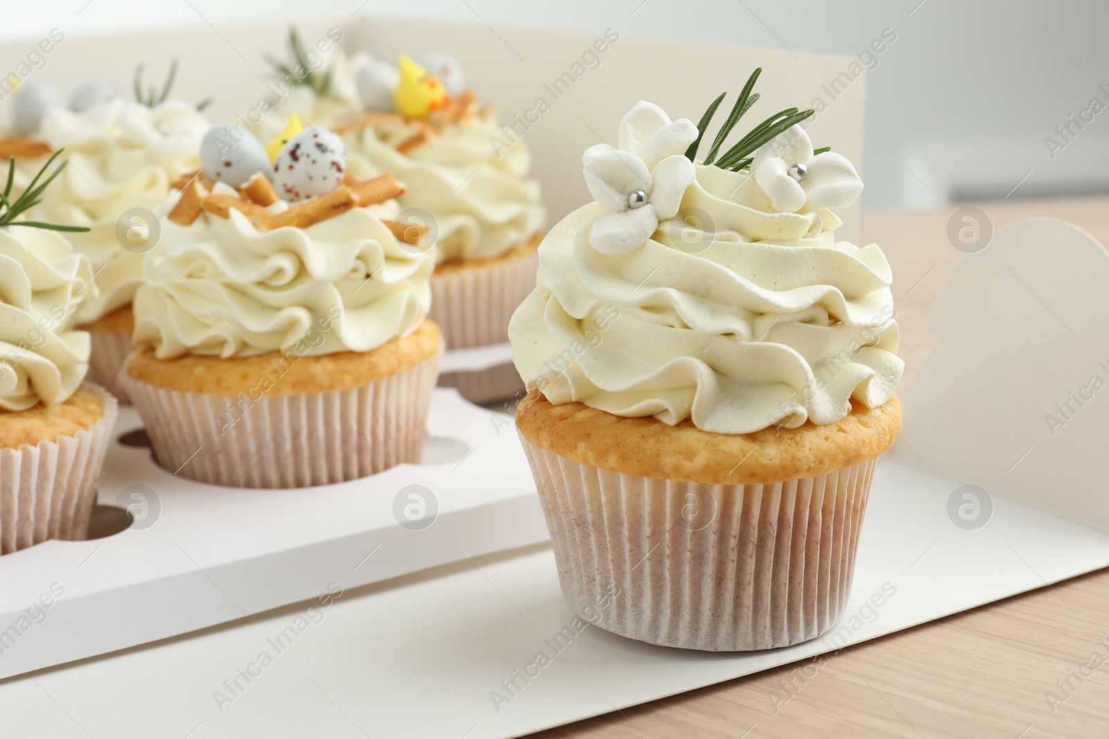 Photo of Tasty Easter cupcakes in box on wooden table, closeup