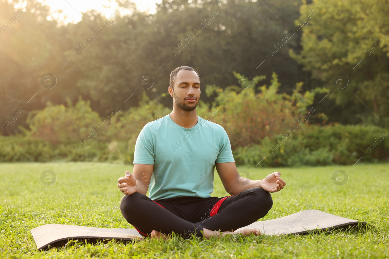 Photo of Man practicing yoga on mat outdoors. Lotus pose