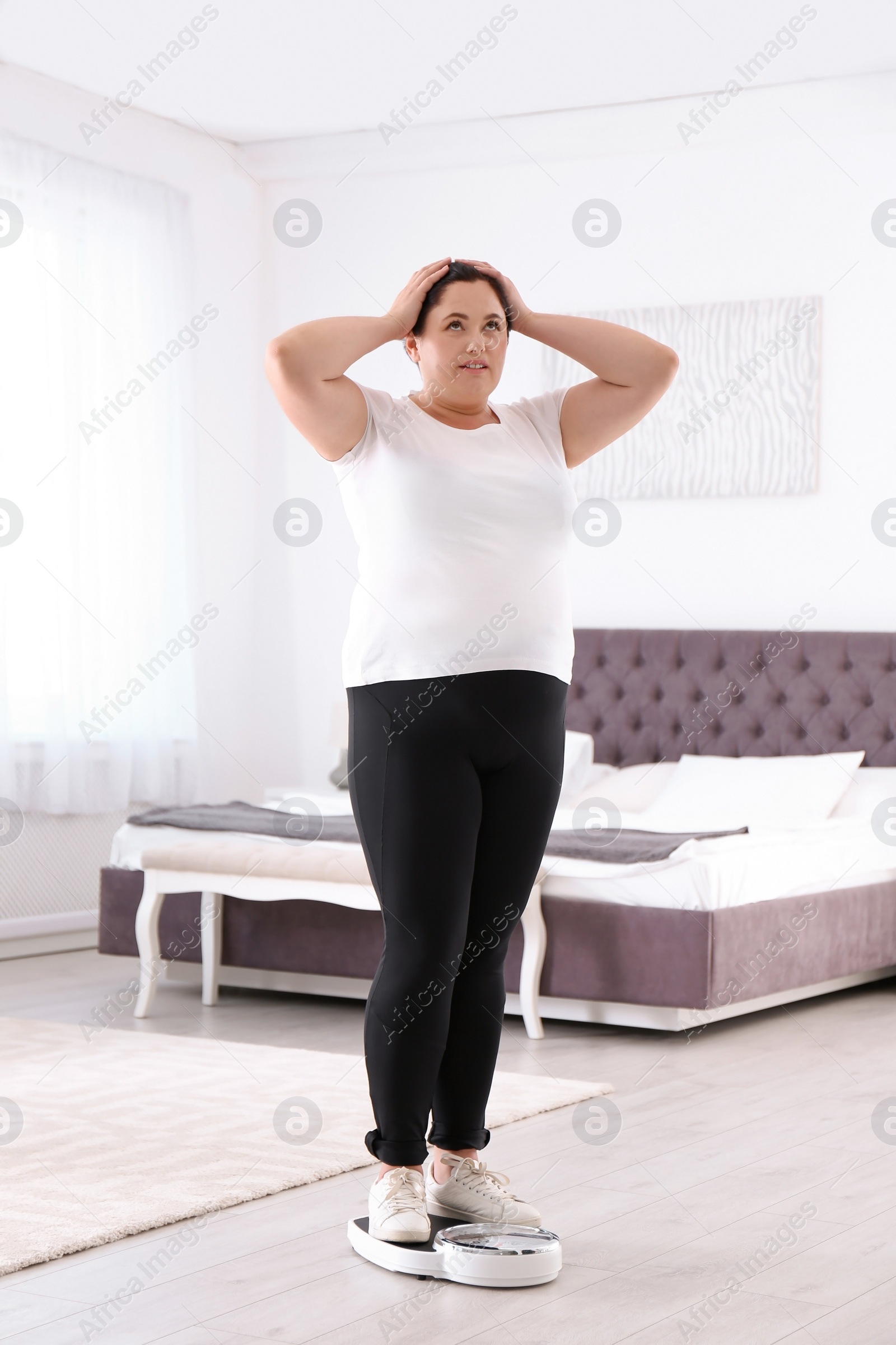 Photo of Overweight woman in sportswear using scales in bedroom