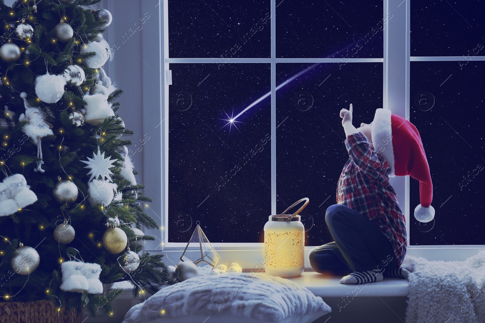 Image of Cute little boy in Santa hat sitting on windowsill and looking at shooting star in beautiful night sky