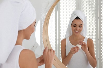 Happy young woman with cream near mirror in bathroom