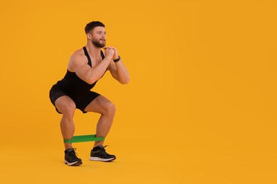 Photo of Young man exercising with elastic resistance band on orange background. Space for text