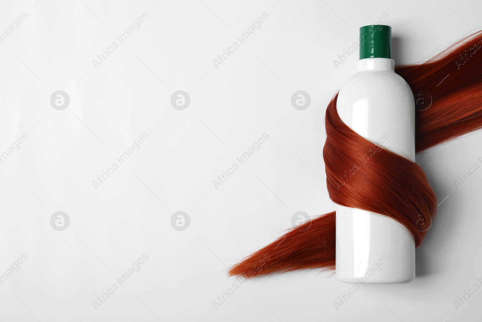 Photo of Shampoo bottle wrapped in lock of hair isolated on white, top view. Natural cosmetic products