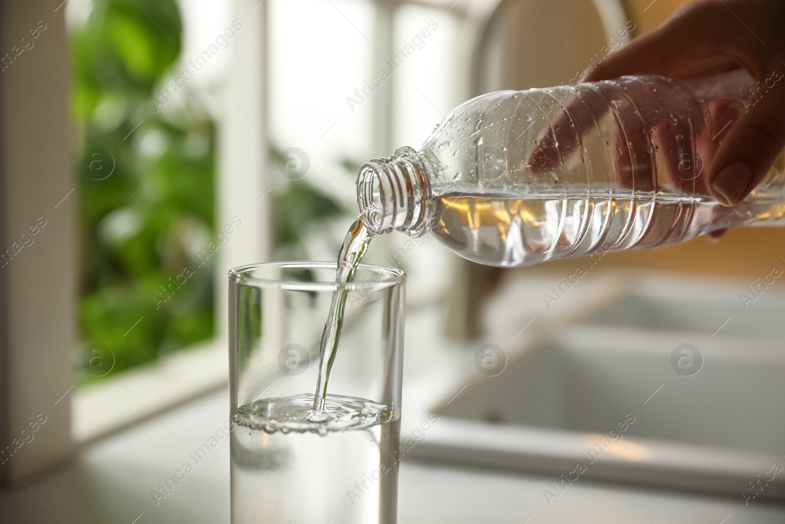 Photo of Woman pouring water from bottle into glass in kitchen, closeup