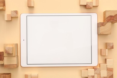Photo of Modern tablet and wooden cubes on beige background, flat lay. Space for text