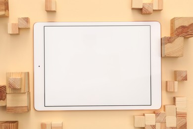 Modern tablet and wooden cubes on beige background, flat lay. Space for text