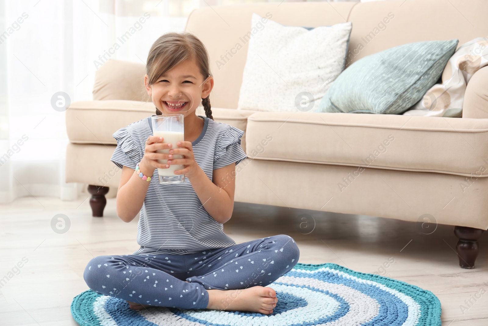 Photo of Cute little girl drinking milk on floor at home