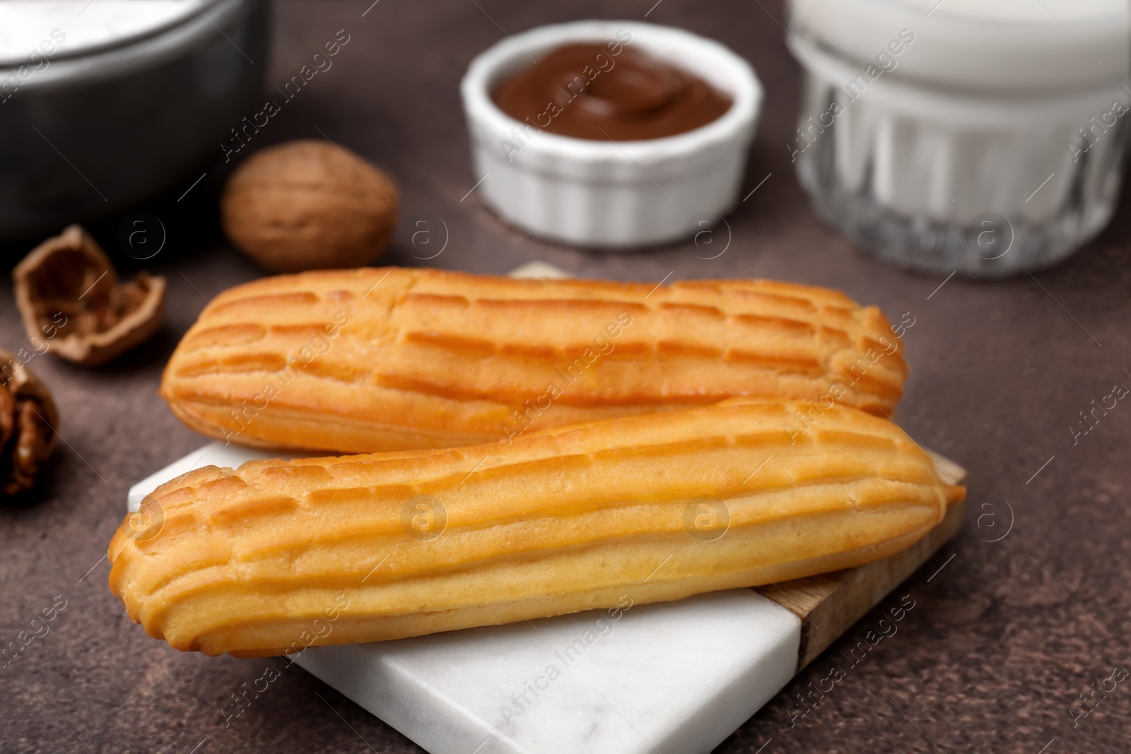 Photo of Delicious eclairs, walnuts and chocolate paste on grey table, closeup