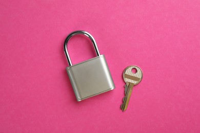 Photo of Modern padlock with key on pink background, flat lay