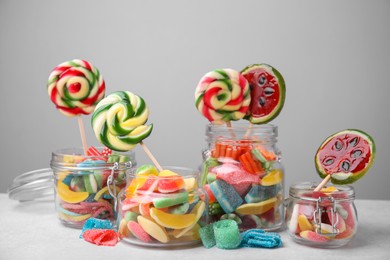 Tasty different candies in jars on light grey table