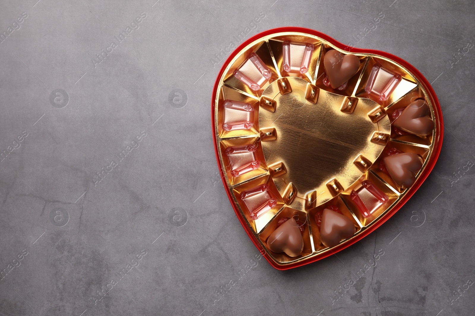 Photo of Partially empty heart shaped box of chocolate candies on grey background, top view. Space for text