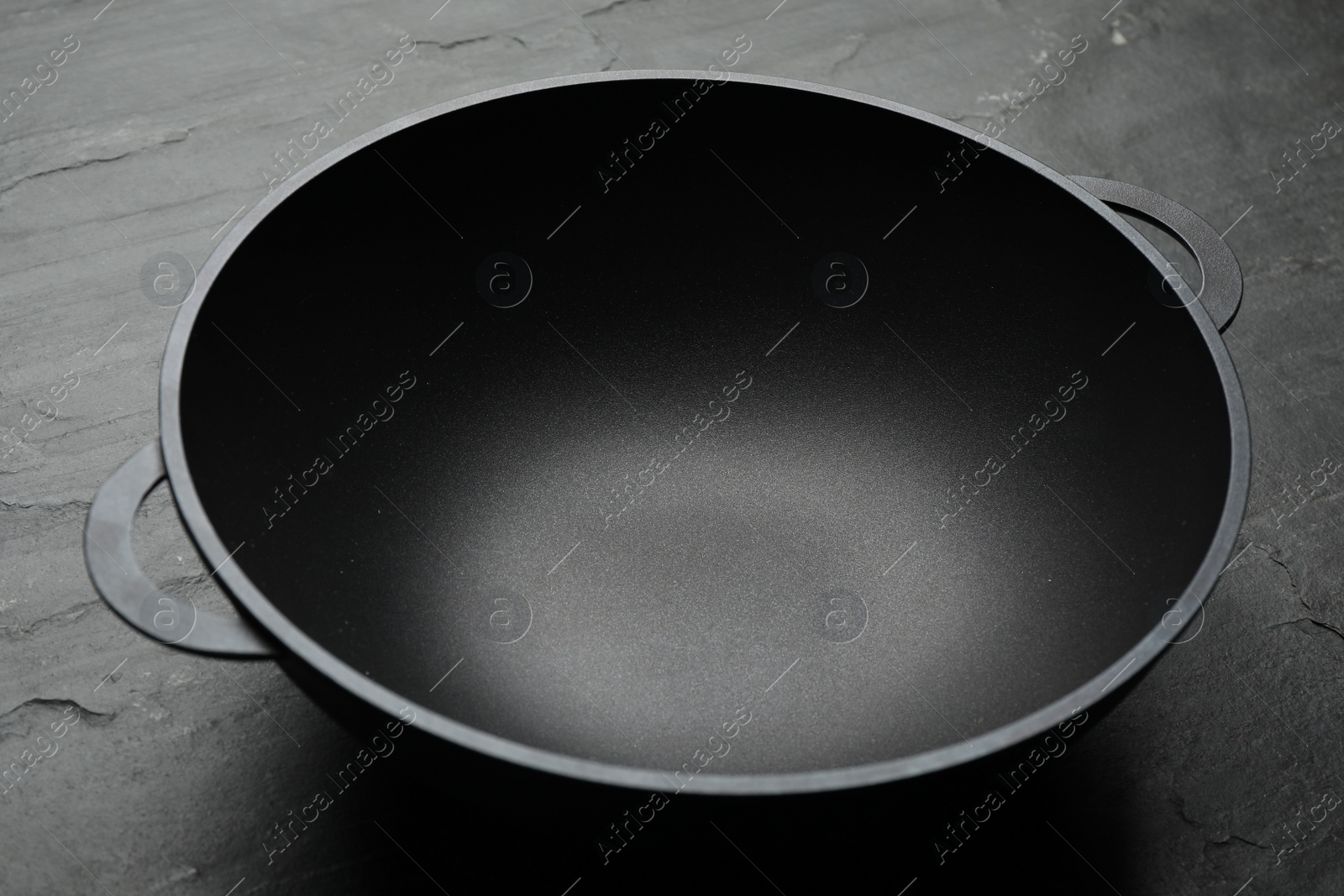 Photo of Empty iron wok on black slate table, closeup. Chinese cookware