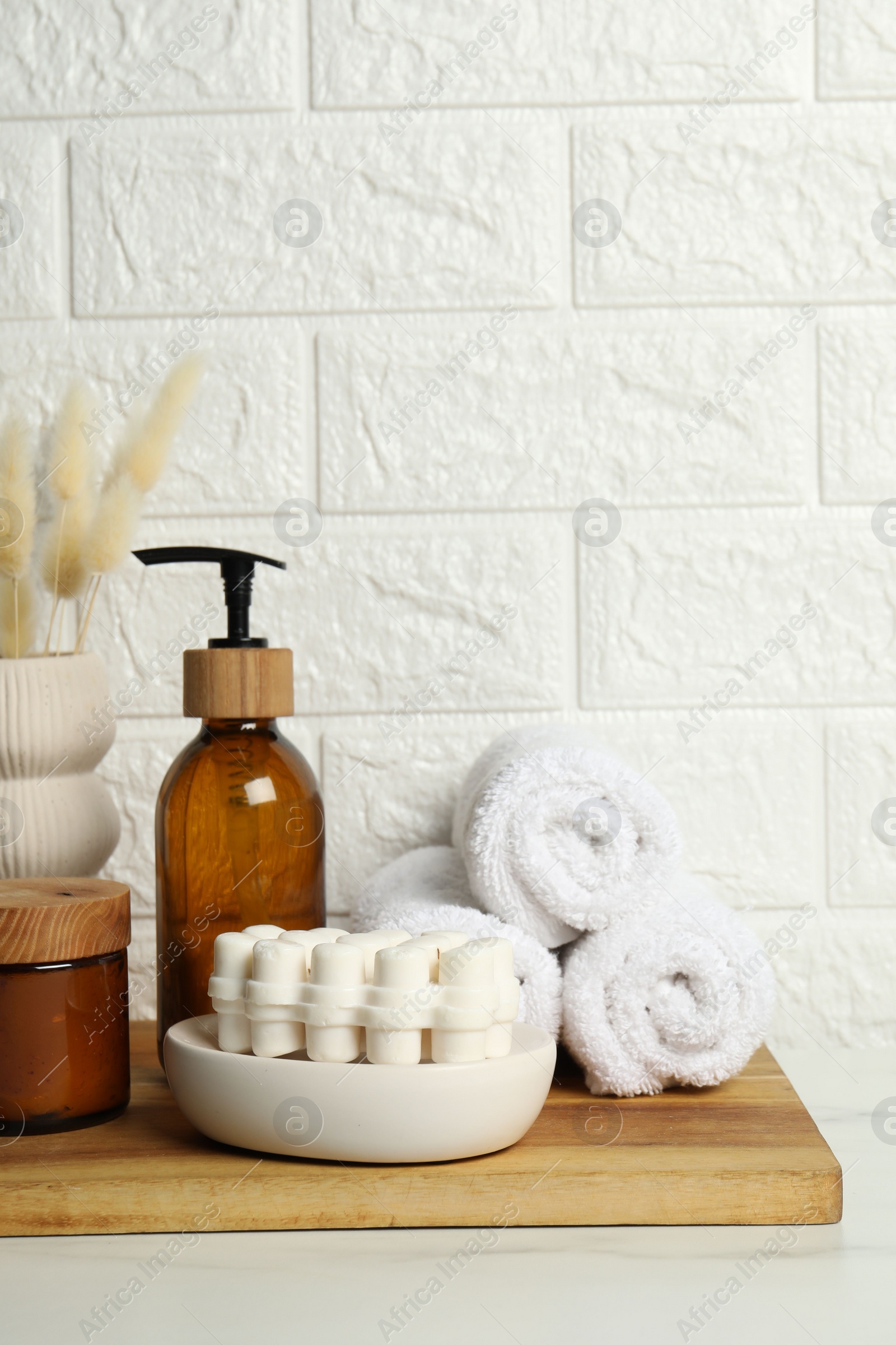 Photo of Different bath accessories, personal care products and spikelets in vase on white table near brick wall